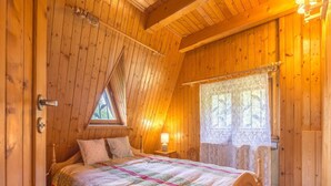 A cozy wooden room with a bed, a window with lace curtains, and a wooden ceiling. - Holiday Home by the Lake, Sauna, Boat, Bicycles (Chmielno)
