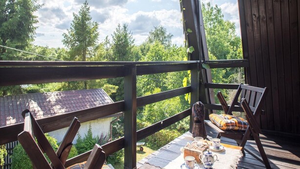 A wooden deck with a table set for tea, surrounded by chairs with plaid cushions, overlooking a forested area. - Holiday Home by the Lake, Sauna, Boat, Bicycles (Chmielno)