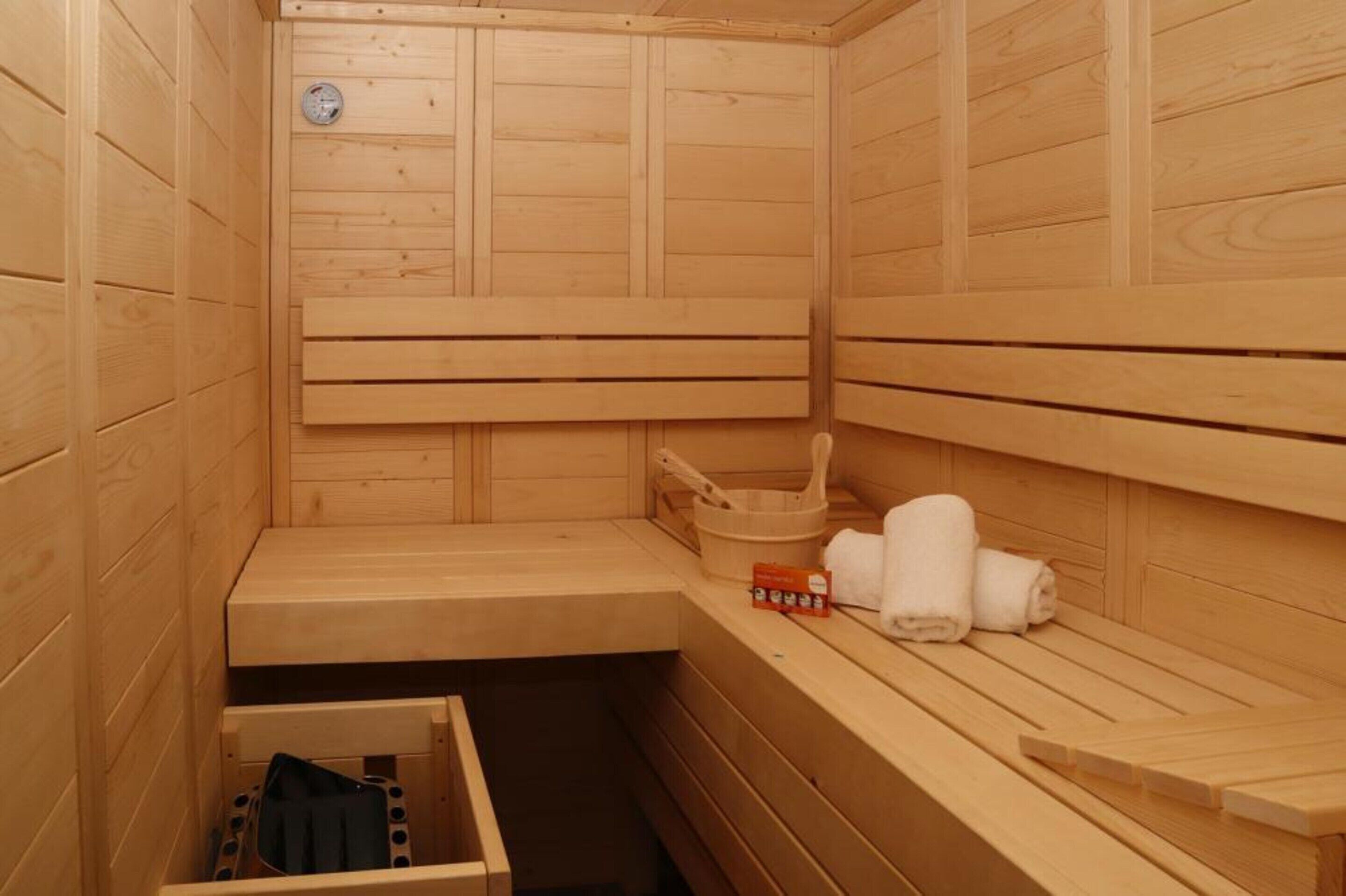 A wooden sauna with benches, a bench with a towel and a box, and a small wooden cabinet.