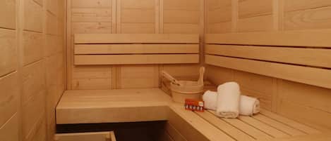 A wooden sauna with benches, a bench with a towel and a box, and a small wooden cabinet.