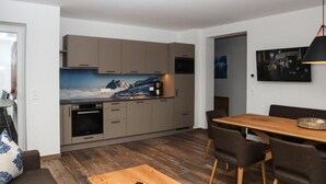 A modern kitchen with grey cabinets, a wooden dining table, and a large painting of a mountain landscape. - Apartment in Bramberg am Wildkogel With Sauna (Bramberg am Wildkogel)