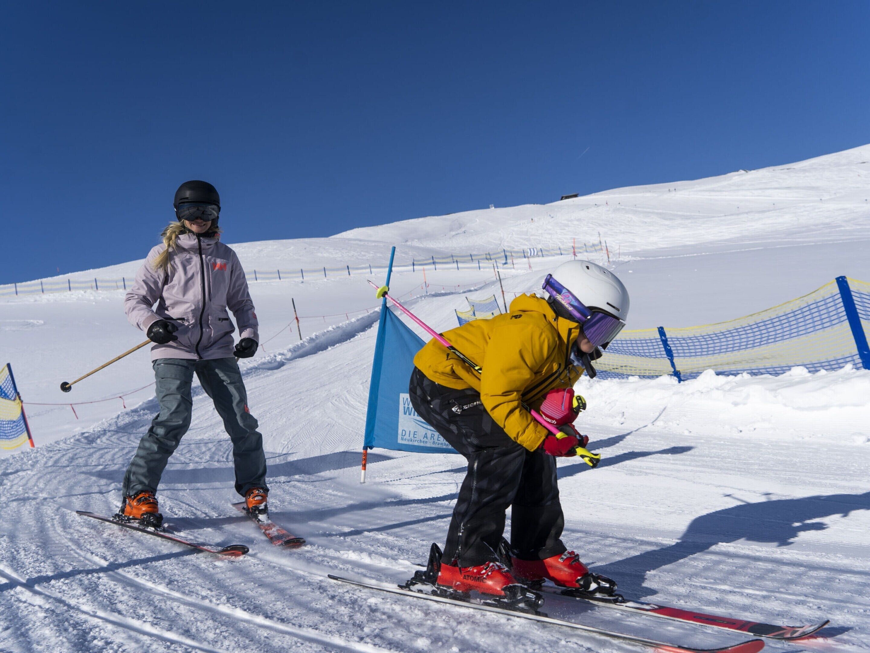 Deux skieurs sur une pente enneigée, sous un ciel bleu dégagé.
