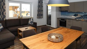 A modern living room with a wooden dining table, a sofa, and a kitchen area with grey cabinets and a blue pendant light. - Apartment in Bramberg am Wildkogel With Sauna (Bramberg am Wildkogel)