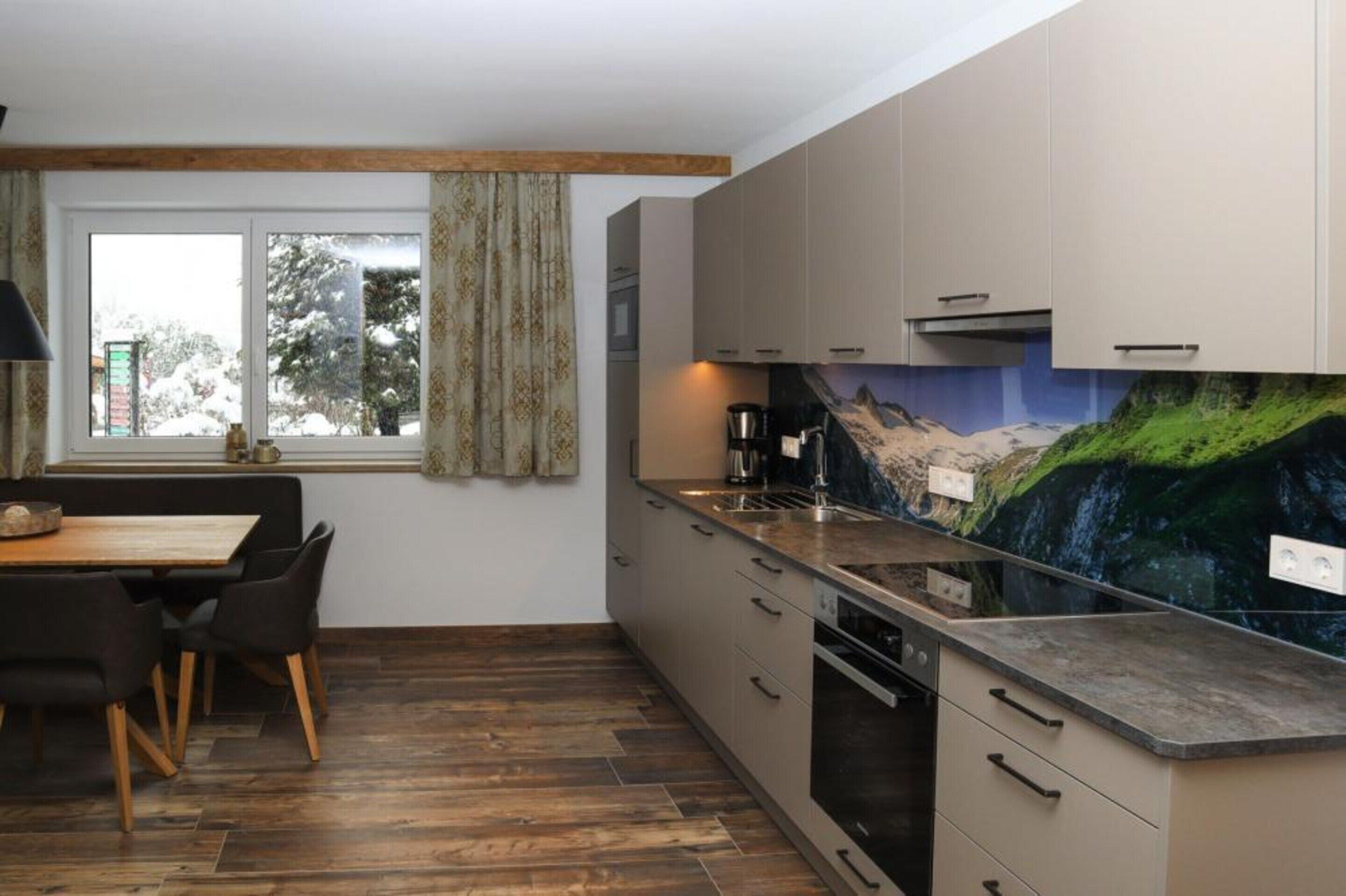 A modern kitchen with a large island, wooden flooring, and a scenic mural on the wall.