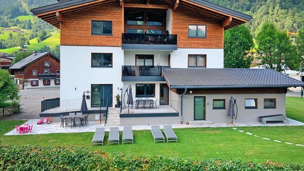 A modern two-story building with a balcony, a small attached structure, and a well-maintained lawn. - Apartment in Bramberg am Wildkogel With Sauna (Bramberg am Wildkogel)