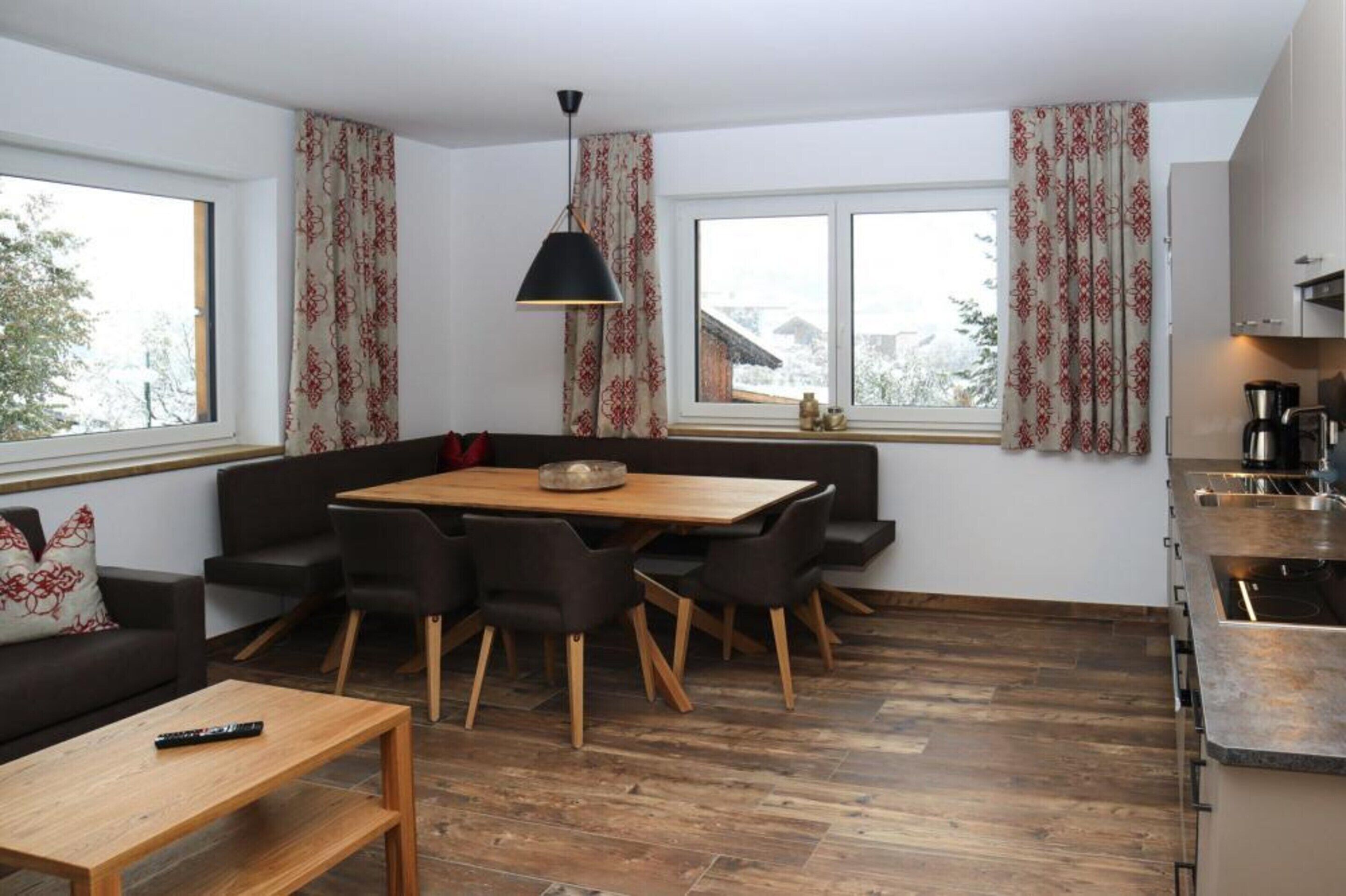 A modern kitchen with a dining area, featuring a wooden table, black chairs, and a black pendant light.