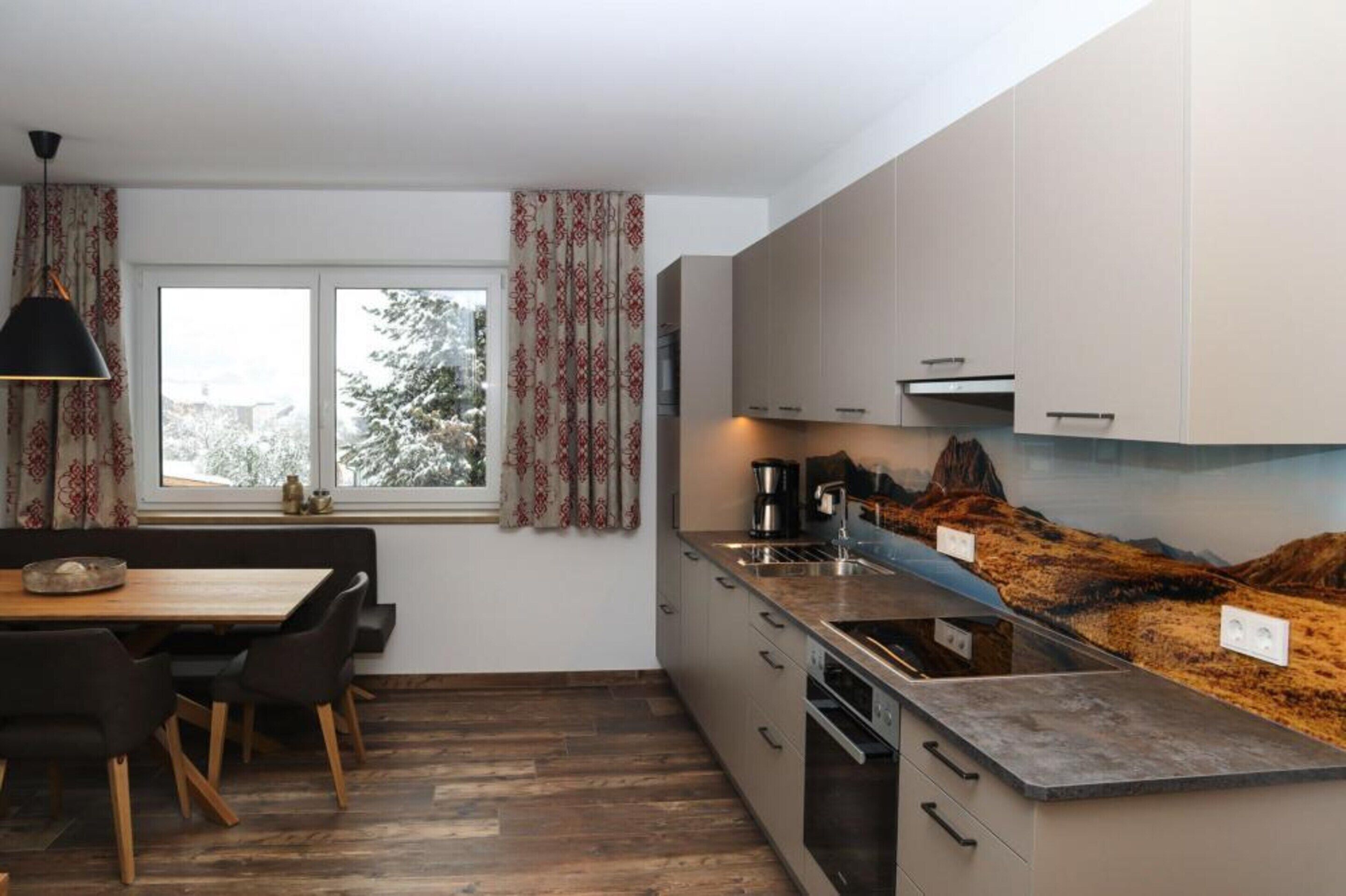 A modern kitchen with a wooden dining table, built-in cabinets, and a large window with curtains.