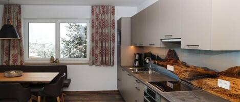 A modern kitchen with a wooden dining table, built-in cabinets, and a large window with curtains.