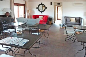 Amplia sala de estar con un sofá rojo, un sofá gris y una mesa de comedor con sillas. Hay un espejo grande en la pared y una planta en maceta en el suelo.