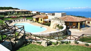 A resort with a swimming pool, multiple buildings with terracotta roofs, and a view of the sea. - Holiday Residence Punta Falcone (Santa Teresa di Gallura)