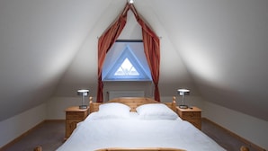 A bedroom with a wooden bed, two bedside tables with lamps, a window with curtains, and a sloped ceiling. - Ferienwohnung Direkt am Deich in St.peter-ording (St. Peter-Ording)