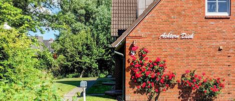 A brick building with a sign reading "Achtern Dick" and a garden with red flowers.