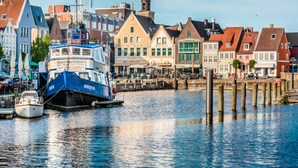 A waterfront with traditional buildings, a docked boat, and wooden pilings. - Ferienwohnung Direkt am Deich in St.peter-ording (St. Peter-Ording)