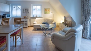 A modern living room with a white sofa, a glass coffee table, and a dining area with a wooden table and chairs. - Ferienwohnung Direkt am Deich in St.peter-ording (St. Peter-Ording)