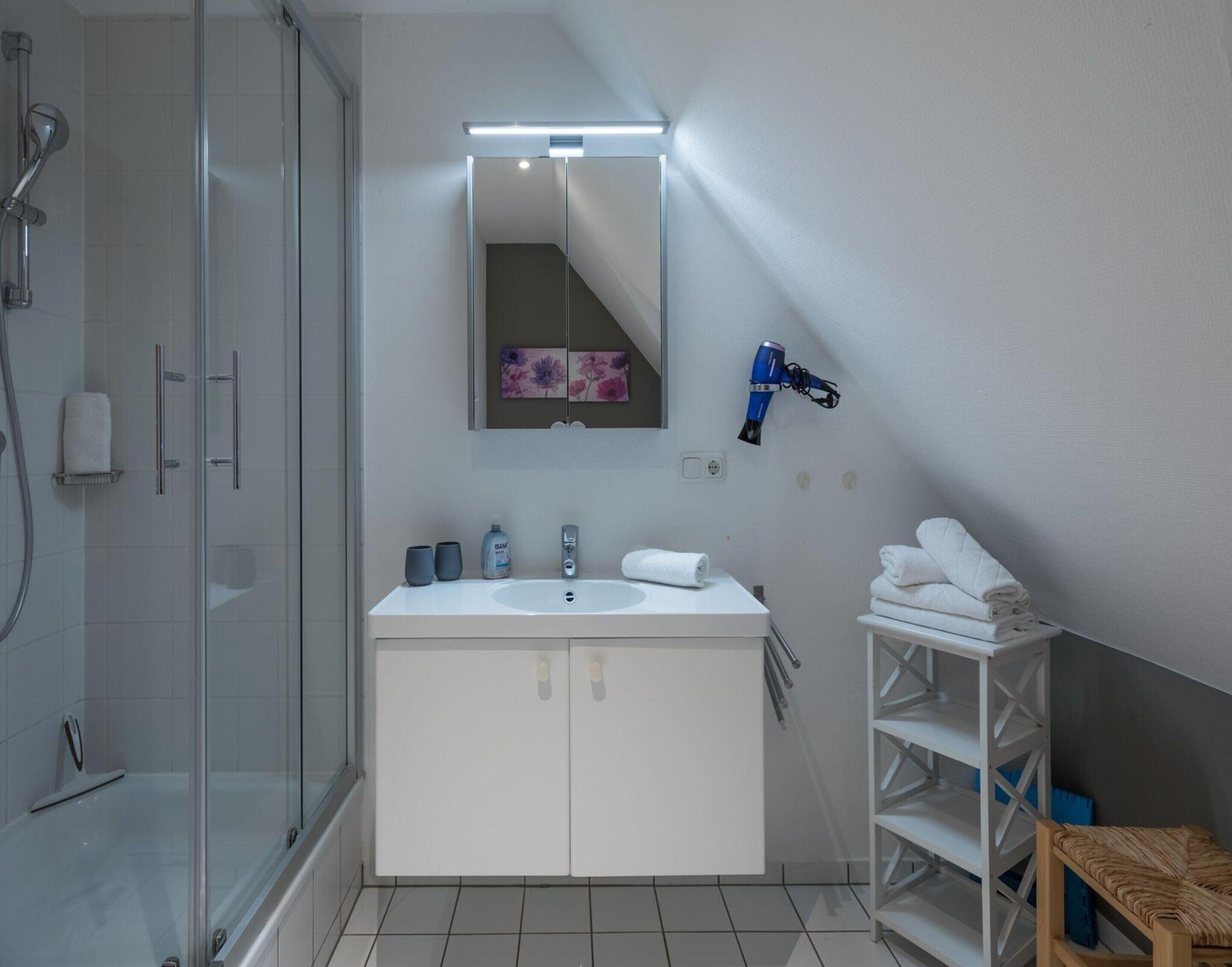A modern bathroom with a glass shower enclosure, a white vanity with a mirror, and a towel rack.