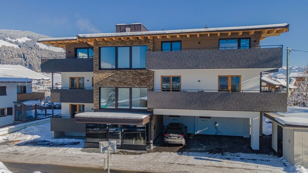 Een modern meerlaags huis met een garage, een auto die erin staat geparkeerd, en een besneeuwd landschap op de achtergrond.