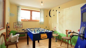 Een gezellige kamer met een tafelvoetbalspel, een PlayStation en een kat op een stoel.