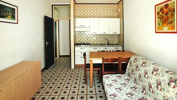 Cozinha compacta com armários brancos, mesa de jantar e sofá estampado.