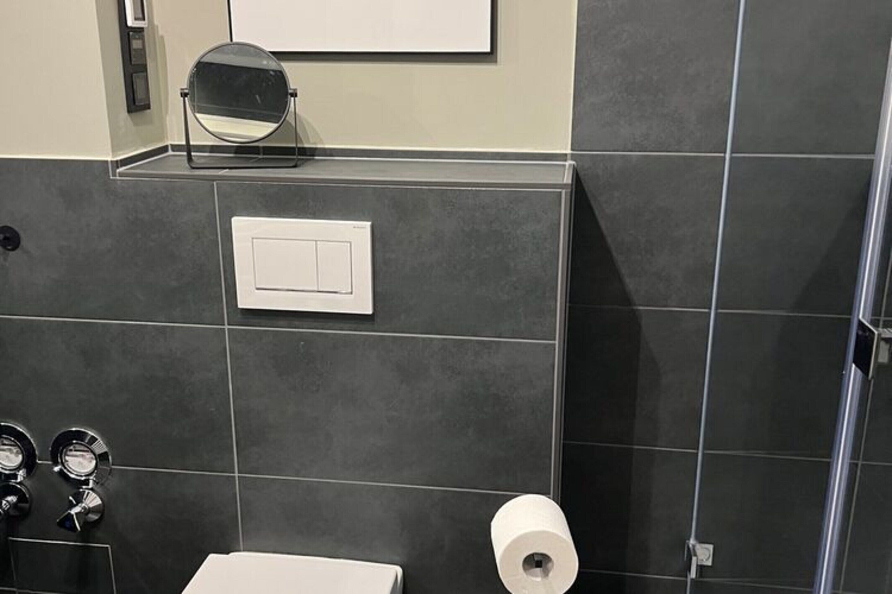 Een badkamer met een toilet, een spiegel, een zeepdispenser en een toiletrolhouder.
