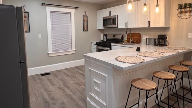 A modern kitchen with white cabinetry, a central island with bar stools, a microwave, stove, and a coffee maker. - Charming 2-bedroom apartment in nice Sharon with WiFi, AC near Gillette Stadium  (Sharon)