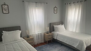 A twin bedroom with two beds, a bedside table with a lamp, and sheer curtains. - Charming 2-bedroom apartment in nice Sharon with WiFi, AC near Gillette Stadium  (Sharon)