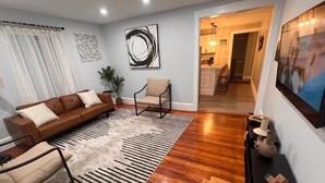 A modern living room with a brown leather sofa, a beige armchair, and a black and white striped rug. There is a painting on the wall and a plant in the corner. - Charming 2-bedroom apartment in nice Sharon with WiFi, AC near Gillette Stadium  (Sharon)