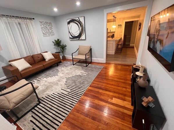 A modern living room with a brown leather sofa, a beige armchair, and a black and white striped rug. There is a painting on the wall and a plant in the corner. - Charming 2-bedroom apartment in nice Sharon with WiFi, AC near Gillette Stadium (Sharon)