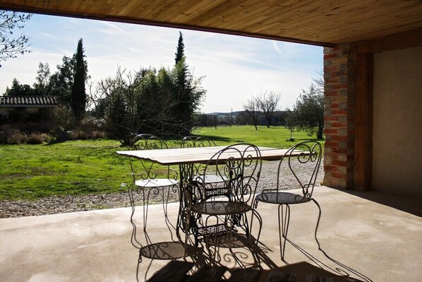 An outdoor patio with a table and chairs, a view of a grassy field, and a brick wall. - 3-star cottage in the countryside with panoramic v (Fiac)