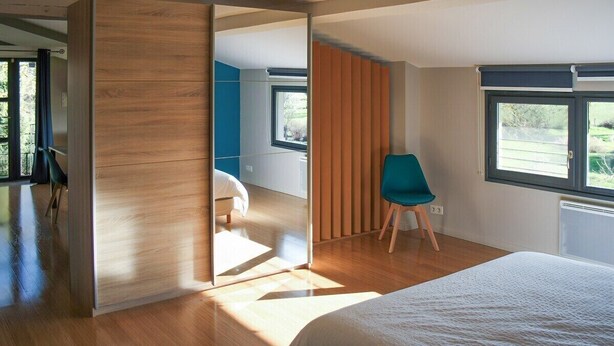 A modern bedroom with a large bed, a sliding door, a window, and a chair. - 3-star cottage in the countryside with panoramic v (Fiac)