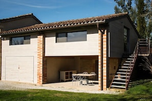 A two-story house with a garage, a covered patio with a table and chairs, and a staircase leading to the upper floor. - 3-star cottage in the countryside with panoramic v (Fiac)