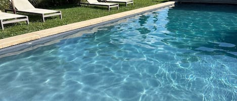 A clear swimming pool with lounge chairs and a wooden deck.