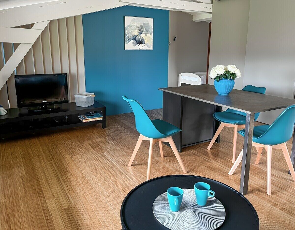 A modern living room with a dining area, featuring a TV, a dining table with chairs, and a small round table with cups.