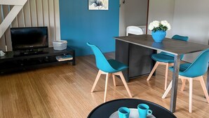 A modern living room with a dining area, featuring a TV, a dining table with chairs, and a small round table with cups. - 3-star cottage in the countryside with panoramic v (Fiac)