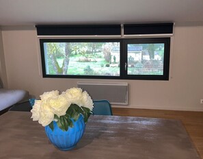 A room with a dining table, a blue vase with white flowers, a window with a view of greenery, and a blue chair. - 3-star cottage in the countryside with panoramic v (Fiac)