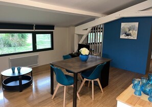 A modern dining area with a dark wooden table, blue chairs, and a vase of white flowers. - 3-star cottage in the countryside with panoramic v (Fiac)