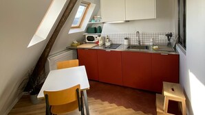 A compact kitchen with a dining area, featuring a wooden table, a small stool, and a red cabinet. - Studio Victoria - Centre de Paris (Paris)
