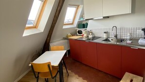 A compact kitchen with a dining area, featuring a small table and chairs, a red countertop, and a window with a view. - Studio Victoria - Centre de Paris (Paris)