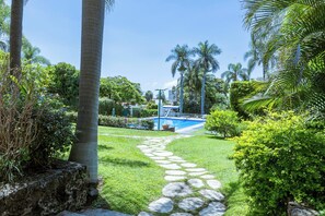 Zona de piscina con un sendero de piedra que lleva a ella, rodeada de vegetación exuberante y palmeras.
