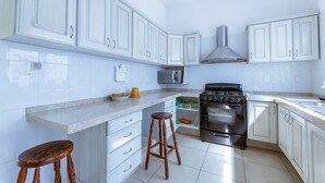 A modern kitchen with white cabinets, a stainless steel stove, a microwave, and a wooden stool. - New house with pool and grill area (Cuernavaca)