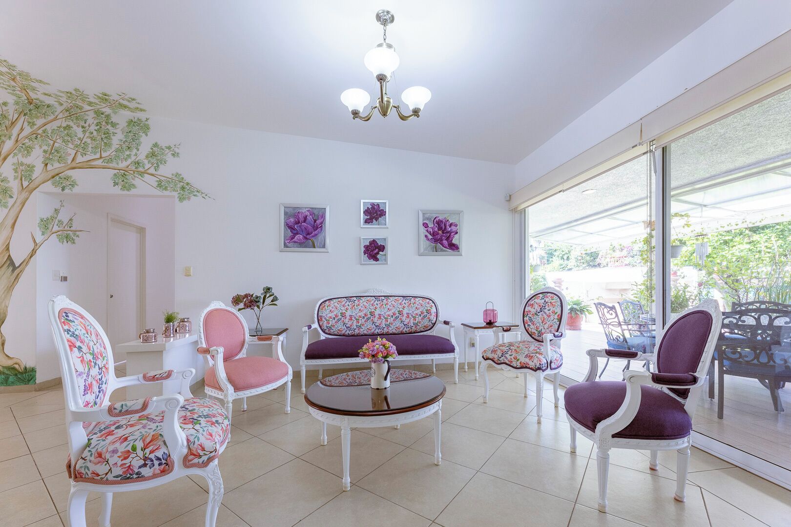 Un salón amplio con muebles blancos, una araña de cristal y ventanas grandes que ofrecen vistas al exterior.