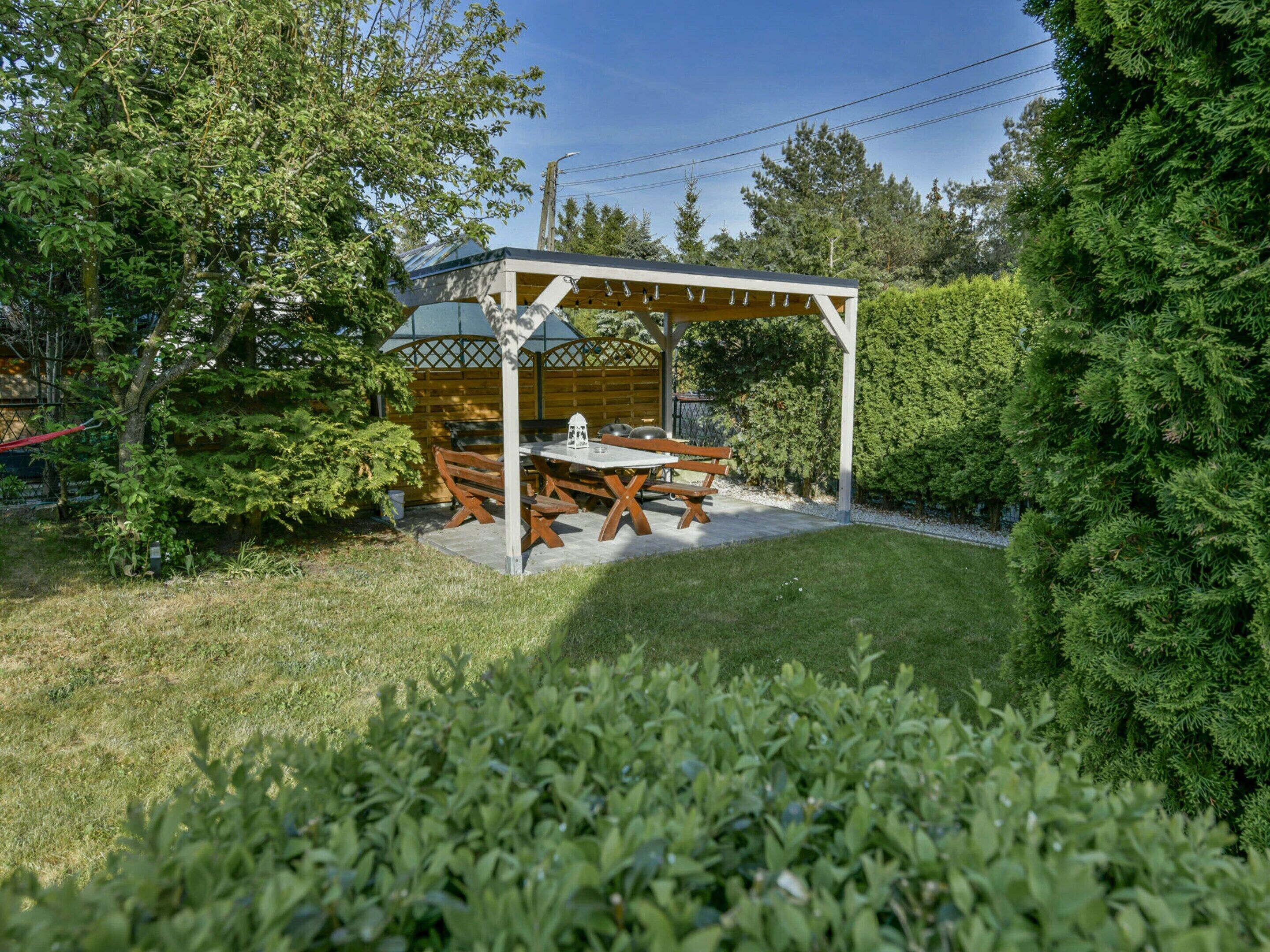 A covered patio area with a table and chairs, surrounded by greenery and trees.