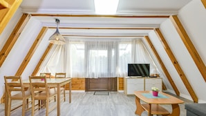 A cozy attic room with a dining table, chairs, a TV, and a sofa. - Holiday Homes With air Conditioning, Large Garden (Kołobrzeg)