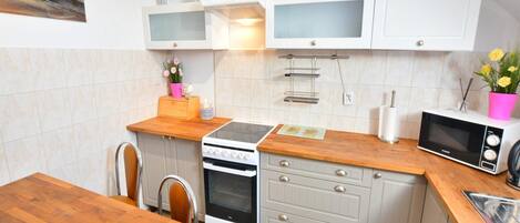 A modern kitchen with white cabinets, a wooden countertop, a stove, an oven, a microwave, and a dining table.