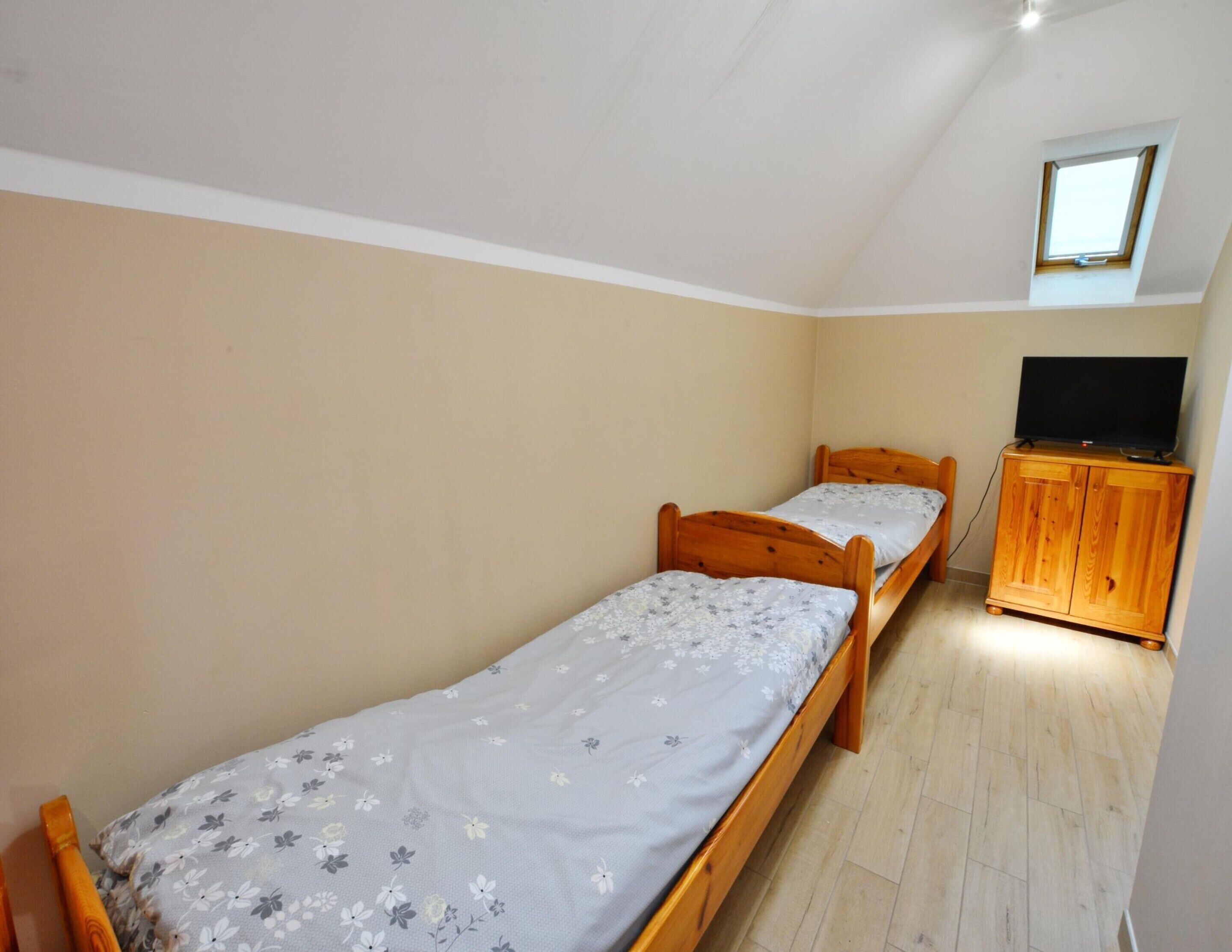 A small, single-room accommodation with two wooden beds, a wooden cabinet, and a television on top.