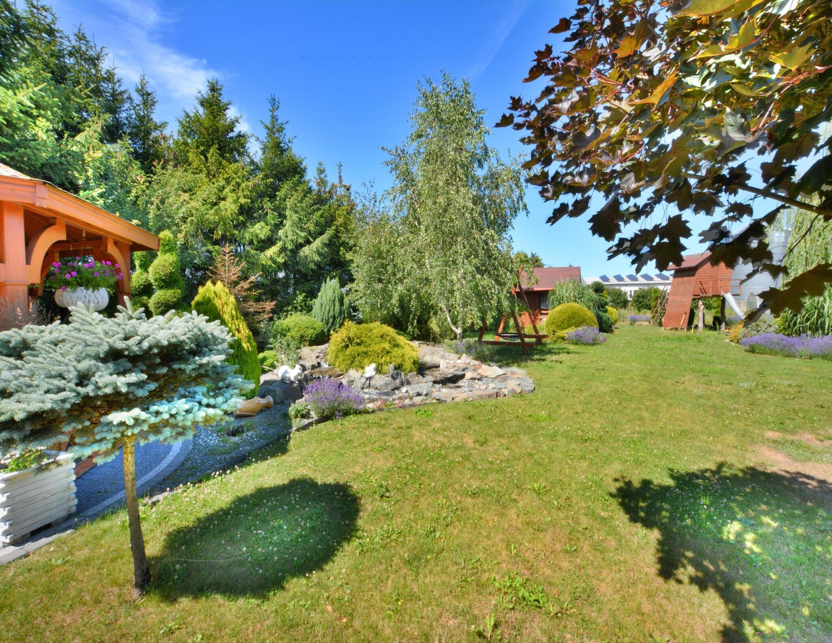 Un jardin bien entretenu, agrémenté d’un bassin, de divers arbustes et d’une structure en bois.