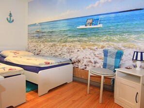 A bedroom with a bed, a chair, a desk, and a wall mural of a beach scene. - Ferienwohnung am Prusssee in Guster (Güster)