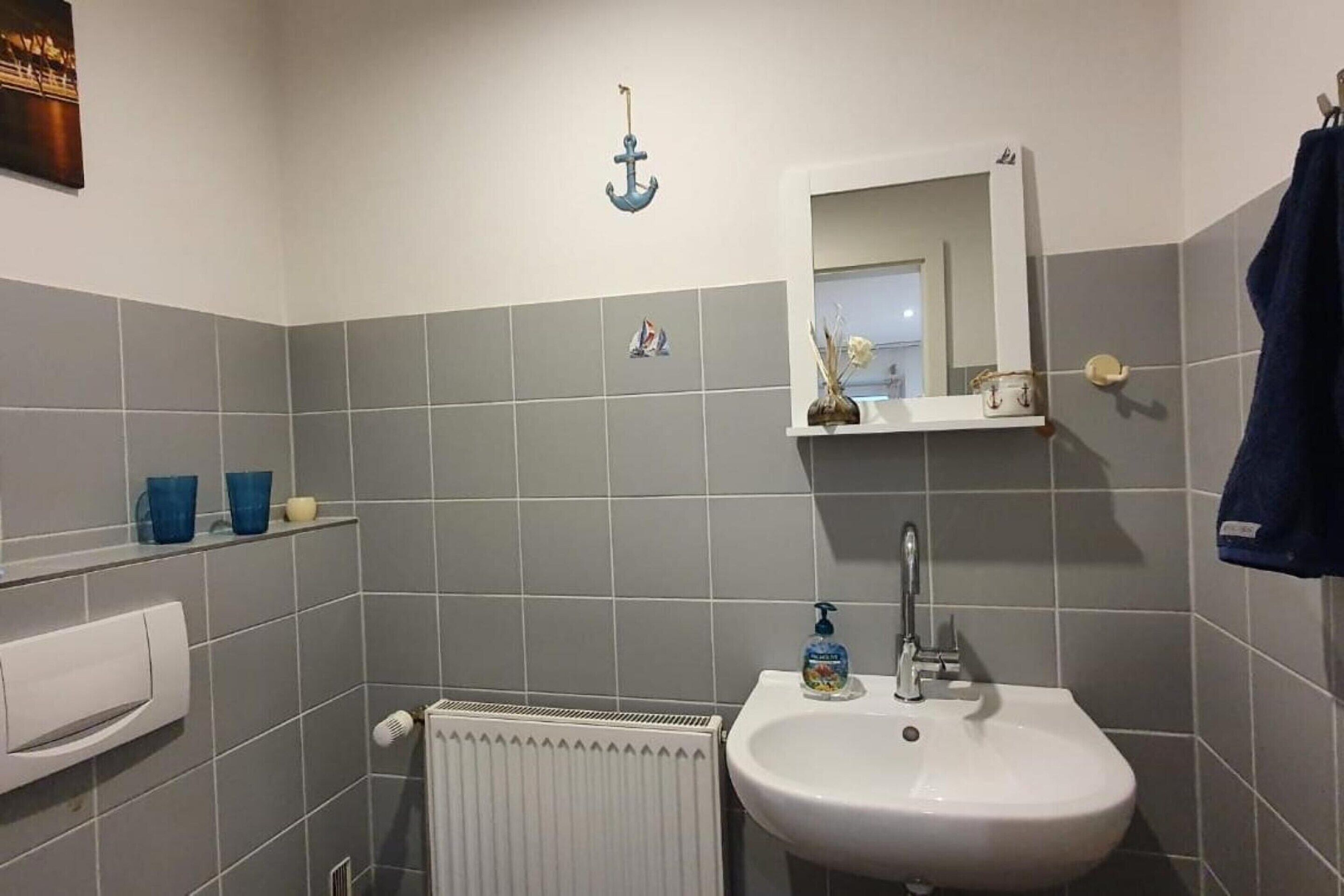 A bathroom with grey tiles, a white sink, a mirror, and a towel rack.