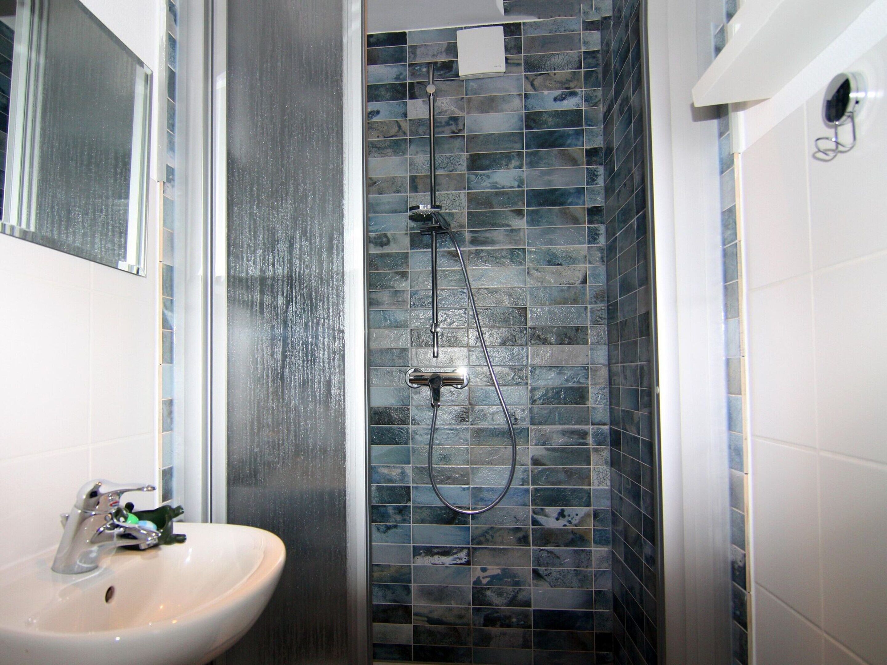 Een badkamer met een wastafel, een douche met een handdouche en een betegelde muur.