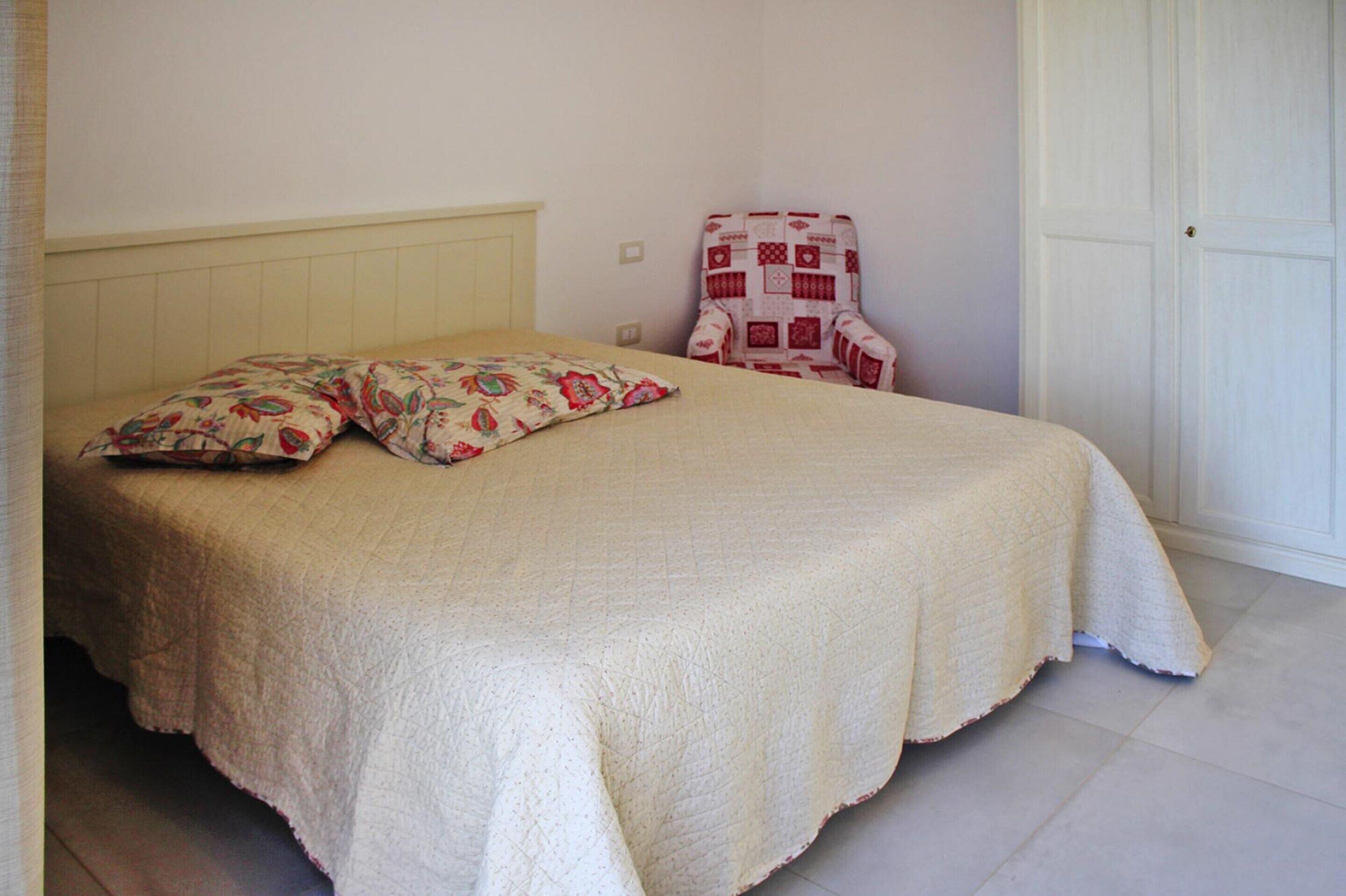 A bed with a quilted cover, a chair with a quilted pattern, and a white door.