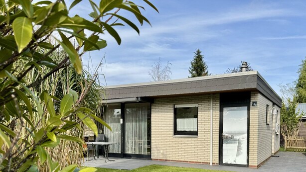 Ein modernes Haus mit flachem Dach, einer Ziegel Fassade und einer kleinen Terrasse mit Tisch und Stühlen.